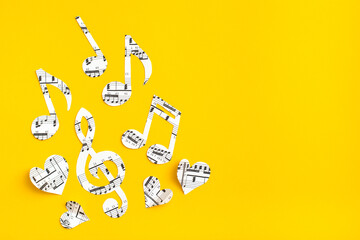 Musical notes, clef and hearts cut from paper with musical text on yellow background. Copy space