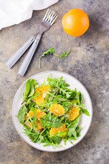 Diet vegetarian vitamin salad of orange pieces and mix of arugula, chard and mizun leaves on a plate on the table. Top and vertical view