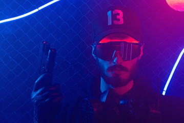 Man with a gun in the neon lights on the night city street. A cyberpunk special force agent concept.