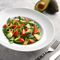 Salad with avocado, lettuce, tomato and flax seeds on gray background.Close up
