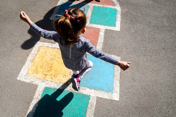 Kid girl 5 y.o. playing hopscotch on playground outdoors