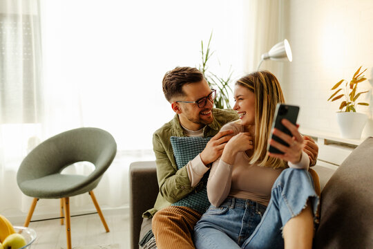 Loving couple sitting on the sofa at home and taking a selfie.