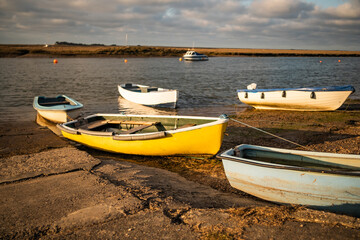 Small pleasure boats beached on the mud at low tide in Wells-Next-The-Sea estuary as the sun starts to set