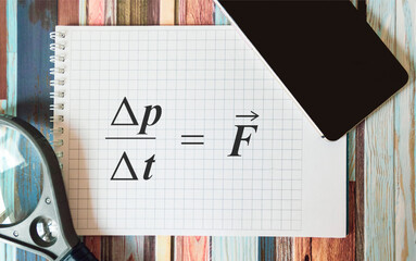 Newton's formula on a notebook, near a magnifying glass and a mobile phone on a striped background.