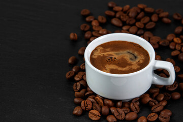 A white cup of coffee with foam on the background of coffee beans scattered on the table