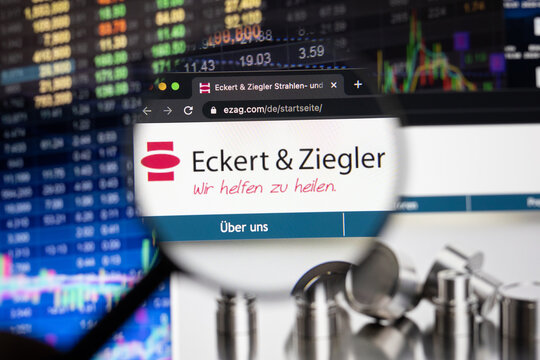 Eckert Ziegler company logo on a website with blurry stock market developments in the background, seen on a computer screen through a magnifying glass