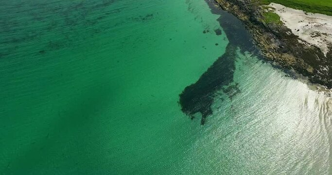 Aerial Panning Gentle Waves Along Remote And Rocky Shoreline With Turquoise Colored Water And Sunlight Reflected Off The Ocean Surface Ripples - Isle of Tiree, United Kingdom