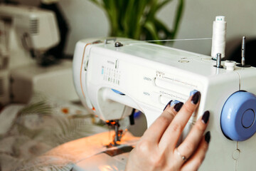 A woman's hand with blue nails adjusts the sewing machine at home. Small business