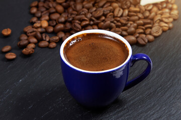 Dark coffee in a blue cup on a background of coffee beans