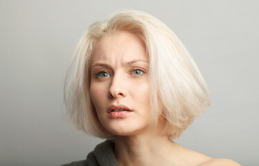 skeptic young beautiful blonde female model on gray background - obrazy, fototapety, plakaty