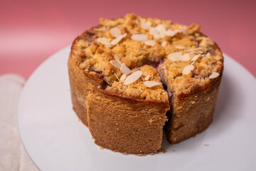 Fototapeta na wymiar A round cake with almonds on a white plate on a pink surface