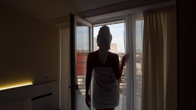 woman in a towel after a bath is standing next to an open door on the balcony