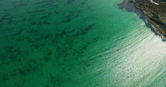 Aerial Panning Ocean Surface Ripples Along Remote And Rocky Shoreline With Turquoise Colored Water And Bright Reflected Sunlight Reflected - Isle of Tiree, United Kingdom