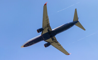 A passenger plane is flying in the sky, leaving a white trail behind it. Close-up of the plane, photographed from below.