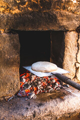 Bread dough on the baker's shovel getting into a rustic oven with embers ready to bake