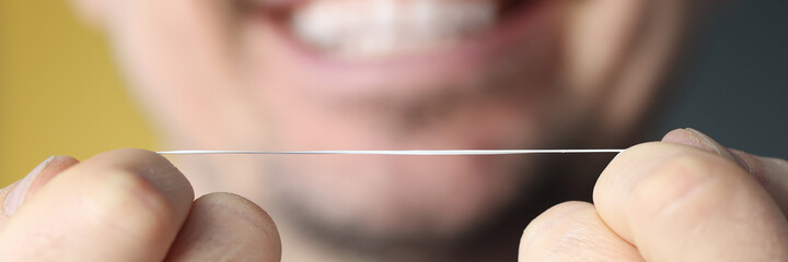 Smiling man holding dental floss in his hands