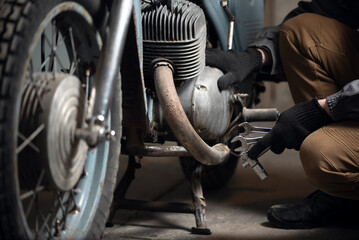 A mechanic is sitting near the motorbike with wrenches in hands close up.