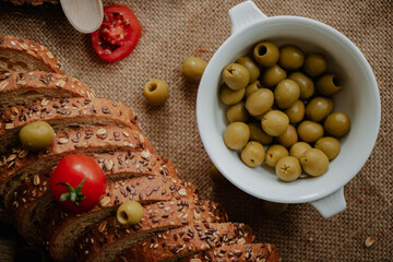Baked sliced bread beautifully placed on a textured surface with cherry tomatoes and olives placed on and around it, nicely decorated in studio environment