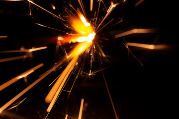horizontal close-up conceptual photography of a bright burning sparkler fire with bright hot orange and yellow sparks trails in the darkness