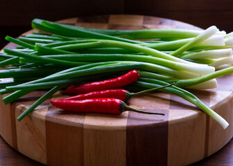 Three small red peppers and green onions on a wooden cutting plate