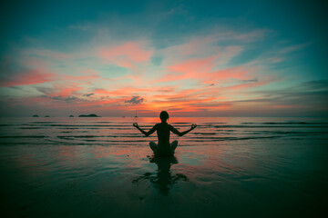 Silhouette of fitnes woman practicing yoga on the sea beach at amazing sunset.