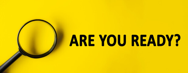 Text ARE YOU READY written over yellow background. Magnifying glass on yellow background. Minimal...