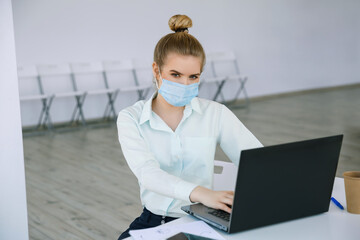 Young beautiful businesswoman works in the protective mask with a laptop