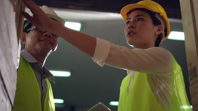 Slow motion Young Asian woman worker use tablet and man engineer supervisor walking to check product box shelf in big warehouse factory store which smile and felling happy, logistic and transportation