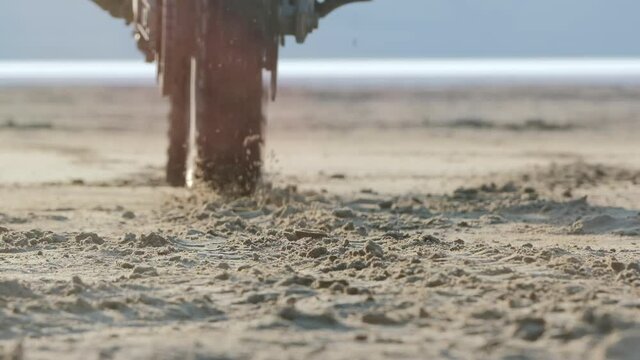 A close-up from a lower view of a motorcycle wheel, moving from a place and picking up sand as it thrusts. The motorcycle starts moving - wheel.