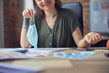 Fototapeta premium Cropped shot of smiling woman, interior designer holding protective mask, working on new project, sitting at the table in her office