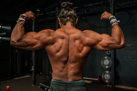 Adult bodybuilder man with long hair showing his back muscles and biceps in a gym