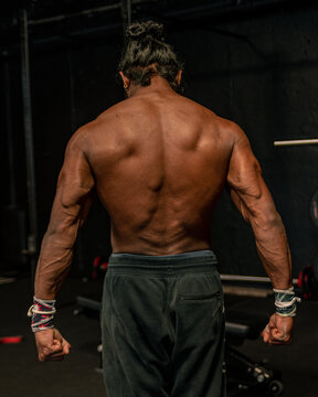 Shallow Focus Of An Adult Bodybuilder Man With Long Hair Showing His Back Muscles In A Gym