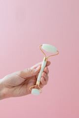 White quartz massager on a woman's hand on a pink background, massager to tighten the skin on the face and neck to eliminate wrinkles and aging effects, taking care of your health, facial skin care