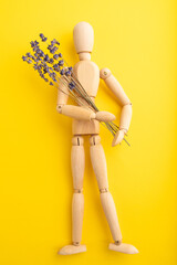 Wooden mannequin holding lavender flowers on yellow pastel background. close up.