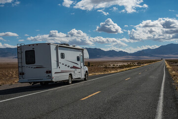 C-type camper with slideouts standing in the desert on the side of the road with mountains in the...