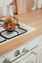 Copper metal retro teapot vintage stands on a gas stove. Boil hot water for tea. An antique item in the apartment. Wooden countertop in the kitchen. Copy space.