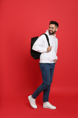 Young man with stylish backpack walking on red background