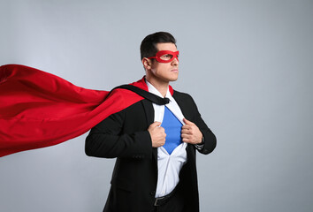 Businessman in superhero cape and mask taking suit off on grey background