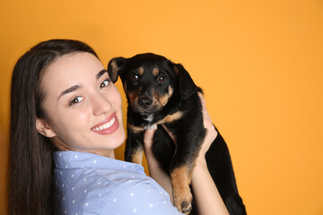 Young woman with cute puppy on yellow background