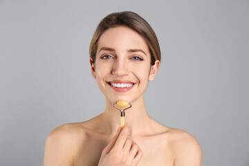 Young woman using natural jade face roller on light grey background