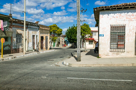 Residential street corner with flat roofed weathered stucco houses, one way street arrow, and local Cubans on sidewalk, Cienfuegos, Cuba.