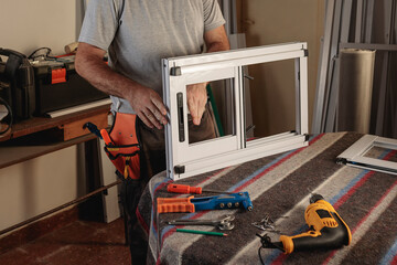 Body part of man working in a carpentry shop. Assembling an aluminum window for a house. Horizontal...