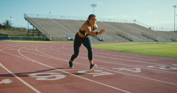 Attractive young woman sprinting down the track at the stadium, epic running workout, fitness lifestyle