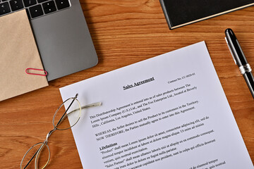 There is a dummy paper of Sales Agreement on the desk with a laptop, a pen and glasses.