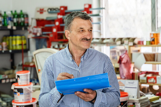 Front View Portrait Of Adult Caucasian Man Senior Entrepreneur At Store Holding Document Writing Or Making A List While Looking To The Side At Hardware Shop Store Real People Small Business Concept