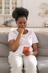 Serious concentrated black woman read message on smartphone. Young pensive female get bad news in...