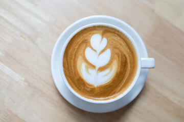 Top view of white cup of hot coffee latte with plate on wooden table.