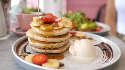Sweet american breakfast. Pouring syrup over stack of fluffy pancakes served with scoop of ice cream and berries 