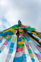 Tibetan religious colored small flags hanging and waving with the wind in Tibet Province during the day with cloudy blue sky. China (Selective focus)