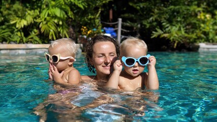 Caucasian Single mom in swimming pool having fun with her twin babies on a sunny day